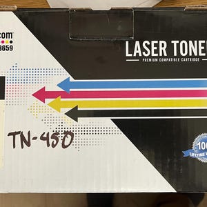 May include: A laser toner cartridge box with the text "LASER TONER" and "PREMIUM COMPATIBLE CARTRIDGE". The box has a color scheme of black, white, blue, pink, and yellow. The text "TN-450" is handwritten on the box.