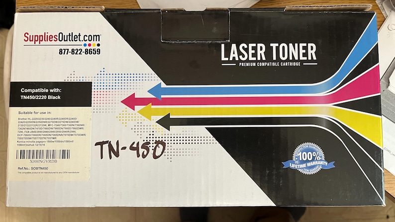 May include: A laser toner cartridge box with the text "LASER TONER" and "PREMIUM COMPATIBLE CARTRIDGE". The box has a color scheme of black, white, blue, pink, and yellow. The text "TN-450" is handwritten on the box.