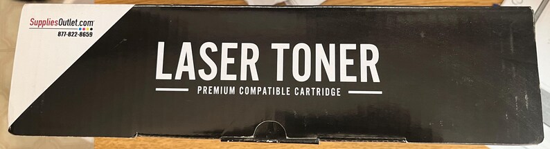 May include: A black box with the words "LASER TONER" in large white capital letters. Below the text is the phrase "PREMIUM COMPATIBLE CARTRIDGE" in smaller white letters. The box has a white and black angled design on the left side.