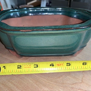 May include: A green glazed ceramic bonsai pot with a rectangular shape and rounded edges. The pot is 5 inches wide and 3 inches deep.