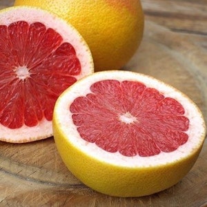 May include: Close-up of sliced grapefruits with vibrant red flesh and yellow rinds. One whole grapefruit is visible in the background. The fruit is cut open, revealing the juicy interior. The image is a food photography shot.