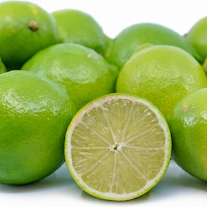 May include: A group of limes, some whole and one cut in half, on a white background. The limes are green and glossy.