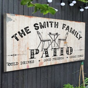 K&ouml;nnte beinhalten: Ein wei&szlig;es Schild mit schwarzem Text, auf dem steht "The Smith Family Patio - Cold Drinks, Good Friends, Great Times". Das Schild zeigt eine Schwarzwei&szlig;illustration eines Tisches und zweier St&uuml;hle.