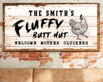 Op de afbeelding: Een wit houten bord met zwarte tekst die "The Smith's Fluffy Butt Hut Welcome Mother Cluckers" luidt. Een zwart-witte illustratie van een kip staat op het bord.