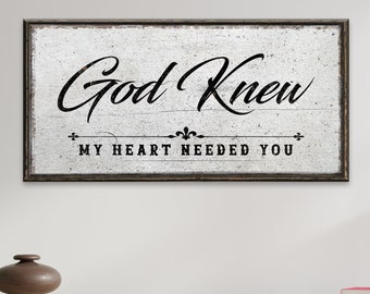 May include: A white wooden sign with black text that reads "God Knew My Heart Needed You". The sign has a distressed look and is framed in a dark wood frame.