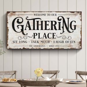 May include: A rustic wooden sign with white paint and black lettering that reads "Welcome to our Gathering Place Sit Long Talk Much Laugh Often The Anderson's Since 1998".