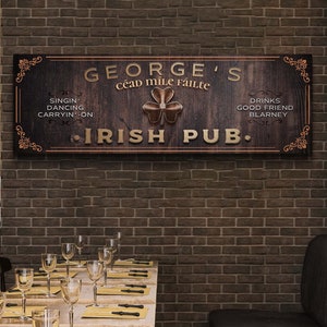 May include: A brown wooden sign with gold lettering that reads "George's Céad Mile Fáilte Irish Pub." The sign has a shamrock design and lists activities like singing, dancing, and drinking.
