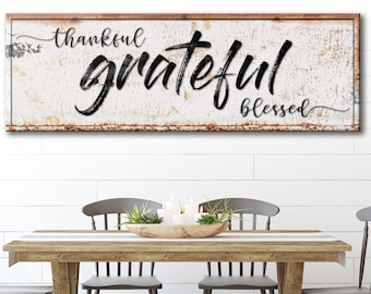May include: A white wooden sign with black lettering that reads "thankful grateful blessed". The sign has a distressed, rustic look with a brown border.