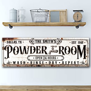 May include: A white sign with black text and a rusty brown border. The sign reads "DALLAS, TX THE SMITH'S EST 1968 POWDER ROOM &bull; OPEN 24 HOURS &bull; WASH RINSE DRY REPEAT".