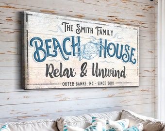 May include: A white wooden sign with blue text that reads "The Smith Family Beach House Relax & Unwind Outer Banks, NC - Since 2001". The sign has a distressed look and features a blue crab illustration.