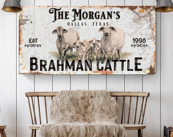 May include: A rustic metal sign with the text "The Morgan's, Dallas, Texas, Est. 1998, Brahman Cattle". The sign features a white background with brown and black text and a faded, distressed look. Five white Brahman cattle are pictured in the center of the sign.