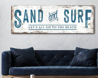 May include: A white wooden sign with blue text that reads "SAND and SURF LET'S ALL GO TO THE BEACH". The sign has a distressed look and is perfect for a beach-themed home.
