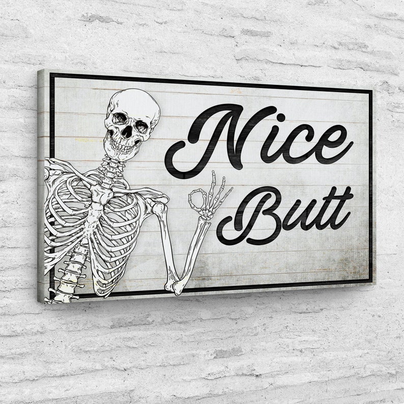 May include: A rectangular canvas art print featuring a black and white skeleton illustration. The skeleton is giving the 'okay' hand gesture. The words "Nice Butt" are written in a bold, black script on a white and gray wooden background.