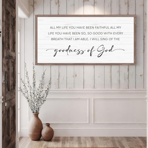 Puede incluir: Un letrero de madera enmarcado con el texto "ALL MY LIFE YOU HAVE BEEN FAITHFUL...goodness of God" en escritura negra. El letrero est&aacute; montado en una pared de tablones blancos. Un jarr&oacute;n con vegetaci&oacute;n y un jarr&oacute;n m&aacute;s peque&ntilde;o est&aacute;n en primer plano.