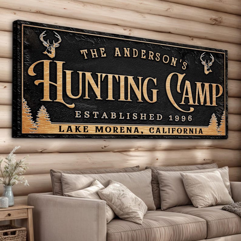 May include: Black wooden sign with gold lettering that reads "The Anderson's Hunting Camp Established 1996 Lake Morena, California". The sign features two deer silhouettes and pine trees.
