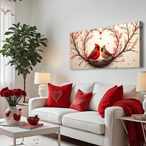 May include: A white couch with red throw pillows and a red blanket. A canvas print of two red cardinals in a nest with pink blossoms hangs above the couch.