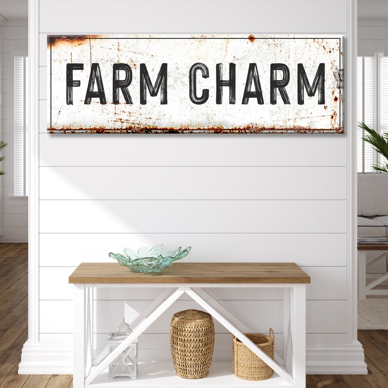 Puede incluir: Un letrero de metal blanco con un aspecto desgastado y oxidado. El letrero dice "FARM CHARM" en letras negras.