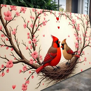 May include: Two red cardinals perched on a nest in a cherry blossom tree. The birds are surrounded by pink blossoms and hearts.