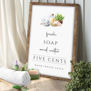 May include: A white sign with a wooden frame, featuring a watercolor illustration of soap, water, and a towel. The sign reads "fresh soap and water FIVE CENTS hand towels extra".
