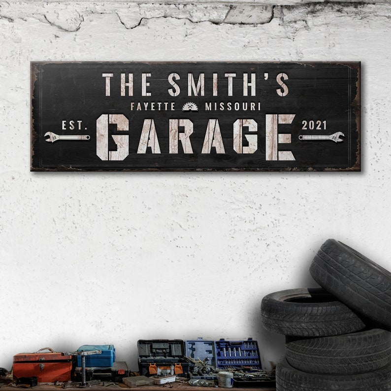 May include: Black wooden sign with white text that reads "The Smith's Garage Est. 2021 Fayette Missouri". The sign has a saw blade icon and wrench graphics.