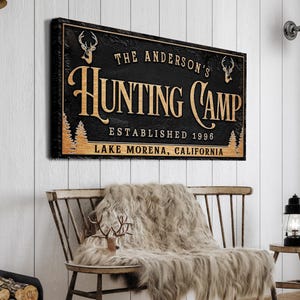 May include: Black and gold sign with the text "The Anderson's Hunting Camp Established 1996 Lake Morena, California" with a deer silhouette on each side.