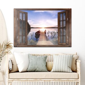 May include: A wooden window frame with a view of a lake at sunset. The lake is calm and the sky is a mix of pink, orange, and blue. A small boat is moored to a wooden jetty that extends into the water.