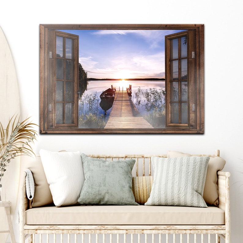 May include: A wooden window frame with a view of a lake at sunset. The lake is calm and the sky is a mix of pink, orange, and blue. A small boat is moored to a wooden jetty that extends into the water.