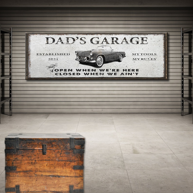 Puede incluir: Un letrero de metal de estilo vintage con el texto "Dad's Garage" y el a&ntilde;o "2021" establecido. El letrero tambi&eacute;n presenta una imagen en blanco y negro de un autom&oacute;vil cl&aacute;sico y el texto "My Tools, My Rules". El letrero tiene un aspecto desgastado y el texto "Open when we're here, Closed when we ain't" est&aacute; escrito debajo del autom&oacute;vil.