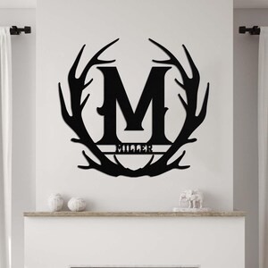 May include: Black metal wall decor featuring a large letter M surrounded by a circle of antlers. The name "Miller" is written below the letter.