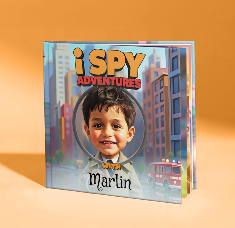 May include: A children's book titled "i SPY Adventures" featuring a cartoon illustration of a smiling child with the name "Martin" below. The cover shows a city scene with a fire truck.
