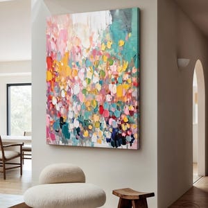 Puede incluir: Lienzo de arte abstracto con una vibrante exhibición de pinceladas coloridas. La obra de arte presenta una mezcla de tonos rosas, amarillos, azules y blancos, creando una composición texturizada y dinámica. La pintura está montada en una pared en un entorno interior moderno.