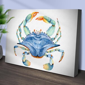 May include: A watercolor painting of a blue crab with orange and green accents. The crab is facing the viewer with its claws raised.