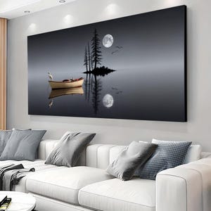 May include: A large canvas print depicting a serene nighttime lake scene. A small boat with a bird floats on the water, reflecting the full moon and silhouetted trees on a small island. The artwork is framed and mounted above a white sofa.