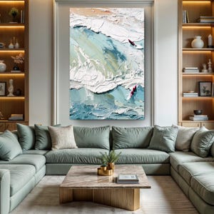 May include: Large abstract oil painting of ocean waves in shades of blue, white, and beige. Two figures on surfboards are visible. The artwork is displayed above a green sectional sofa in a living room.