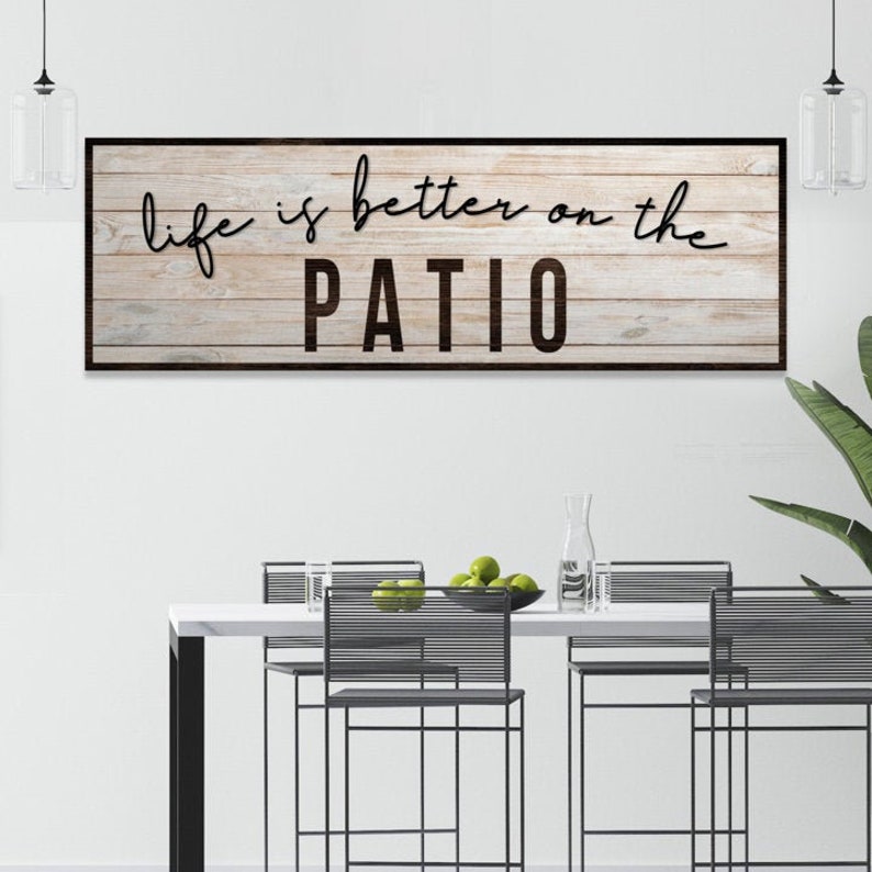 Backyard Patio Lake House wall sign of personalized "Life is Better on the Patio" script on a rustic wood grain panel-inspired canvas with solid black frame.