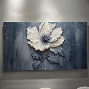 May include: A large, textured wall art piece featuring a white flower with a dark blue center and leaves against a blue-gray background. The flower is the focal point, with detailed petals and a raised, three-dimensional effect. The artwork is rectangular.
