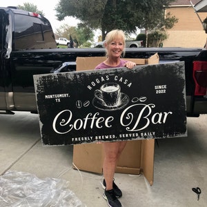 May include: A black and white sign with the text "Rogas Casa Coffee Bar" and the words "Montgomery, TX" and "Since 2022". The sign also features a drawing of a coffee cup and saucer.
