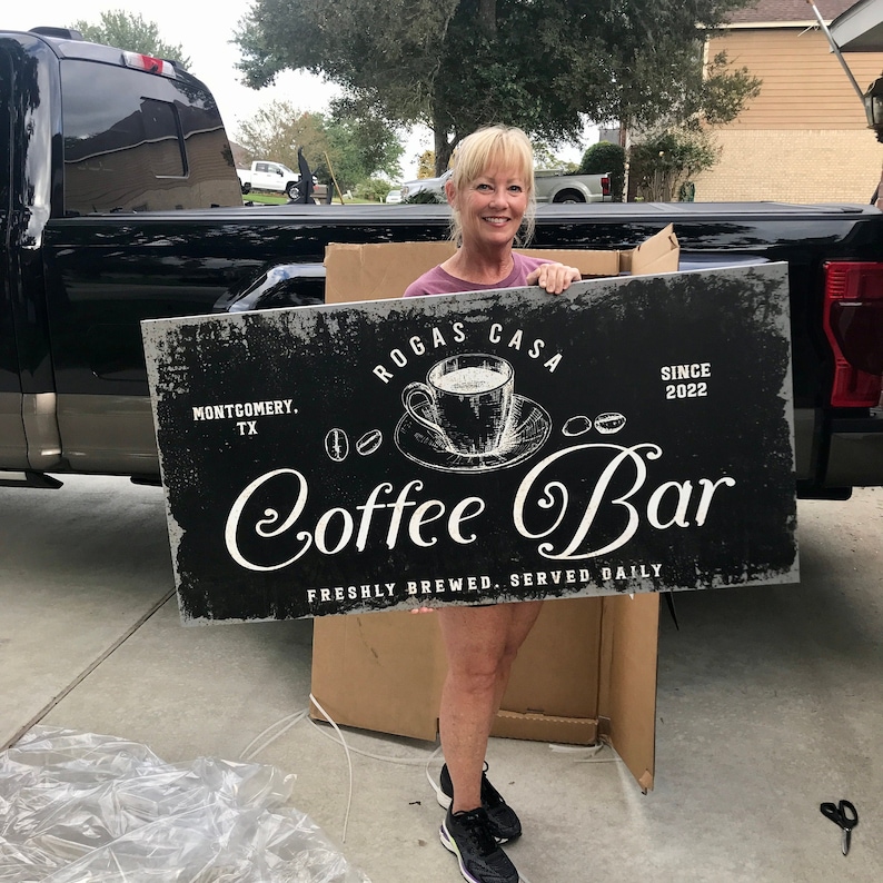 May include: A black and white sign with the text "Rogas Casa Coffee Bar" and the words "Montgomery, TX" and "Since 2022". The sign also features a drawing of a coffee cup and saucer.