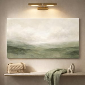 May include: An abstract landscape painting in shades of green and white hangs above a shelf. A beige quilted handbag with a gold chain strap and a green fringed throw blanket are on the shelf. A gold light fixture is above the painting.
