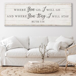 K&ouml;nnte beinhalten: Ein rechteckiges Holzschild mit dem Text "WHERE You GO, I WILL GO AND WHERE You Stay, I WILL STAY RUTH 1:16" in schwarzer Schrift. Das Schild ist &uuml;ber einem wei&szlig;en Sofa mit mehreren Kissen angebracht. Ein runder geflochtener Couchtisch und ein Teppich befinden sich vor dem Sofa.