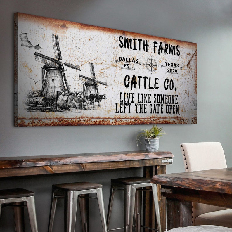 May include: Rustic metal sign with a white background and brown rust accents. The sign features a black and white illustration of two windmills and cattle. The text on the sign reads "Smith Farms, Dallas Est. Texas 2020, Cattle Co., Live Like Someone Left The Gate Open."