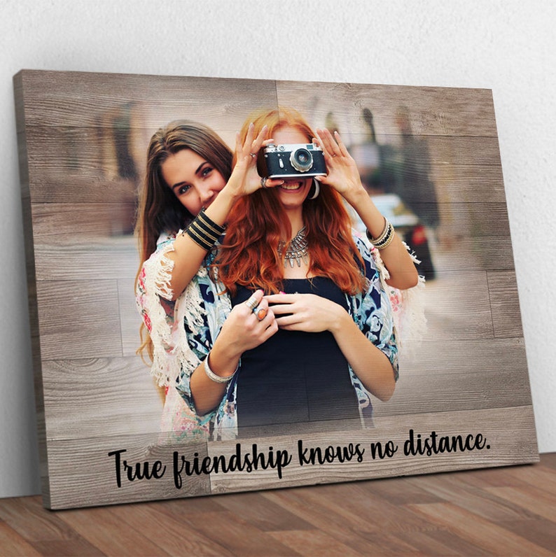 May include: Two friends pose for a photo, one holding a vintage camera up to their face. The image is printed on a wood-grain background with the text "True friendship knows no distance."