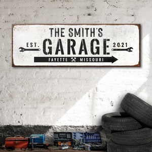 Puede incluir: Se&ntilde;al de metal blanco con texto negro que dice "The Smith's Garage Est. 2021 Fayette Missouri" con iconos de llave inglesa a cada lado del texto.