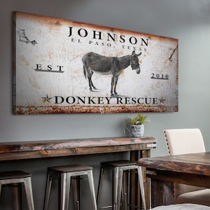 May include: Rustic metal sign with a distressed white background featuring a donkey, the text "JOHNSON EL PASO, TEXAS EST 2010 DONKEY RESCUE", and a star.