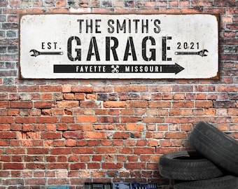 May include: White metal sign with black text that reads "The Smith's Garage Est. 2021 Fayette Missouri" with wrench icons on either side of the text. The sign is hanging on a brick wall.