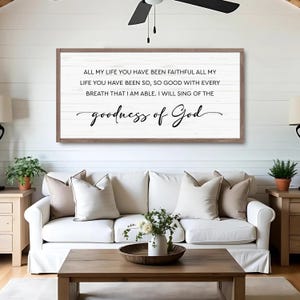 Puede incluir: Un letrero de madera enmarcado con el texto "ALL MY LIFE YOU HAVE BEEN FAITHFUL...goodness of God" en escritura negra. El letrero cuelga sobre un sof&aacute; blanco con cojines beige, una mesa de centro de madera y plantas en macetas.