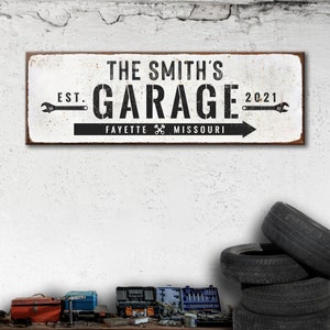 Puede incluir: Un letrero de metal blanco con texto negro que dice "The Smith's Garage Est. 2021 Fayette Missouri" con iconos de llave inglesa a cada lado del texto.