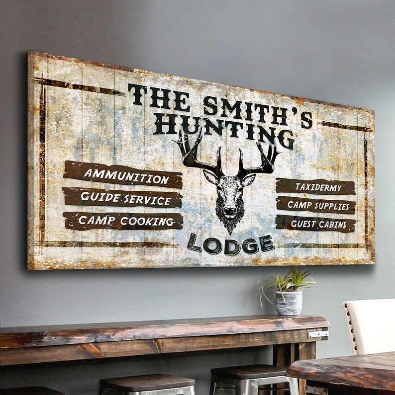 May include: A rustic wooden sign with the text "The Smith's Hunting Lodge" in black lettering. The sign features a deer head illustration and a list of services offered: Ammunition, Guide Service, Camp Cooking, Taxidermy, Camp Supplies, and Guest Cabins.