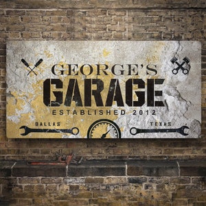 May include: A rectangular garage sign with the text "GEORGE'S GARAGE" in black, established in 2012. The sign has a distressed, weathered look with yellow and gray tones, and includes wrench and screwdriver graphics.
