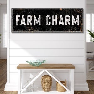 Puede incluir: Un letrero en blanco y negro con el texto "FARM CHARM" en una fuente desgastada. El letrero est&aacute; colgado en una pared blanca de tablones de madera sobre una mesa de madera con un cuenco de vidrio y dos cestas tejidas.